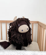 Fergus the Highland cow soft toy standing in a timber cot, showing his cream horns and muzzle