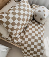 Bedroom with a rattan headboard, khaki gingham duvet cover and a dice cushion beside a locker
