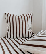 Square chocolate and ivory striped euro pillowcase propped in the corner of a bed