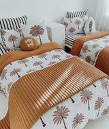 Two beds with striped euro pillowcases, palm print bedding and a tobacco corduroy quilt