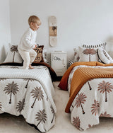 Child standing on a bed in a kids room dressed with striped euro pillowcases and palm print bedding