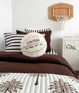Kids bed with a striped pillowcase, chocolate duvet, palm print quilt and a basketball cushion