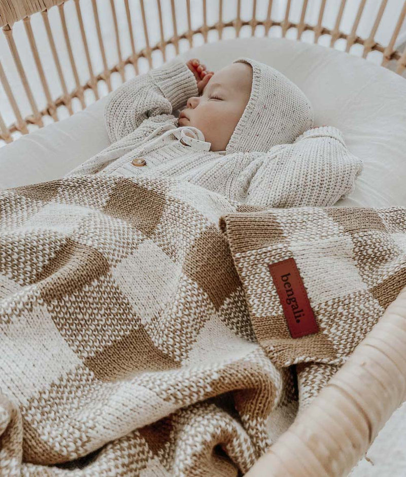 A baby sleeping in a wicker basket with a Bengali Collections KHAKI GINGHAM BLANKET.