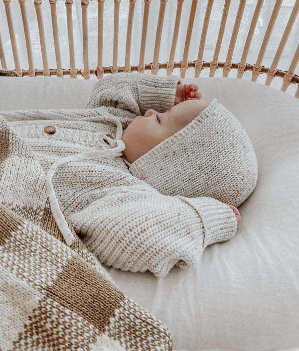 A baby sleeping in a wicker basket with a Bengali Collections KHAKI GINGHAM BLANKET.