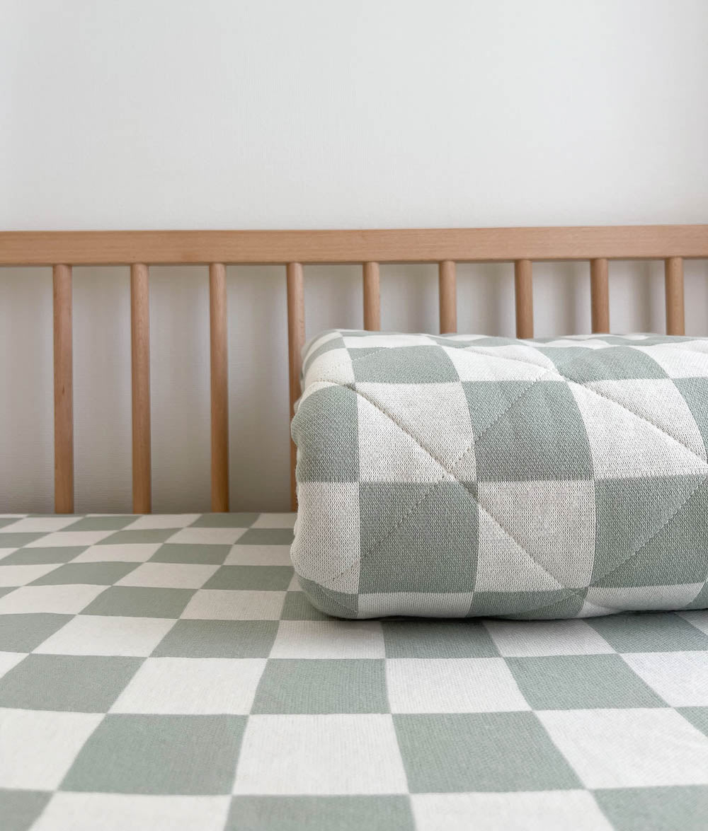 Rolled Sage Gingham reversible quilt on a Sage Gingham jersey cot sheet in a timber cot