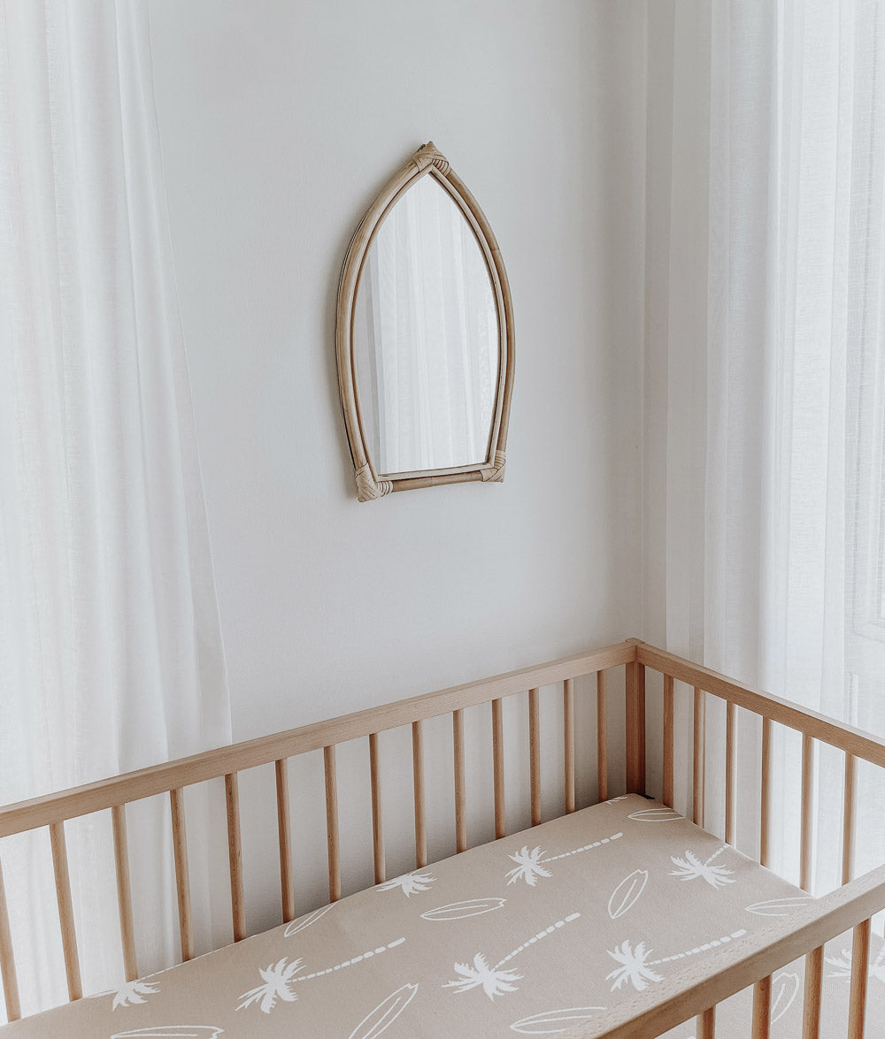 Timber cot with a sand Surfing Palm jersey cot sheet beneath a surfboard-shaped rattan mirror