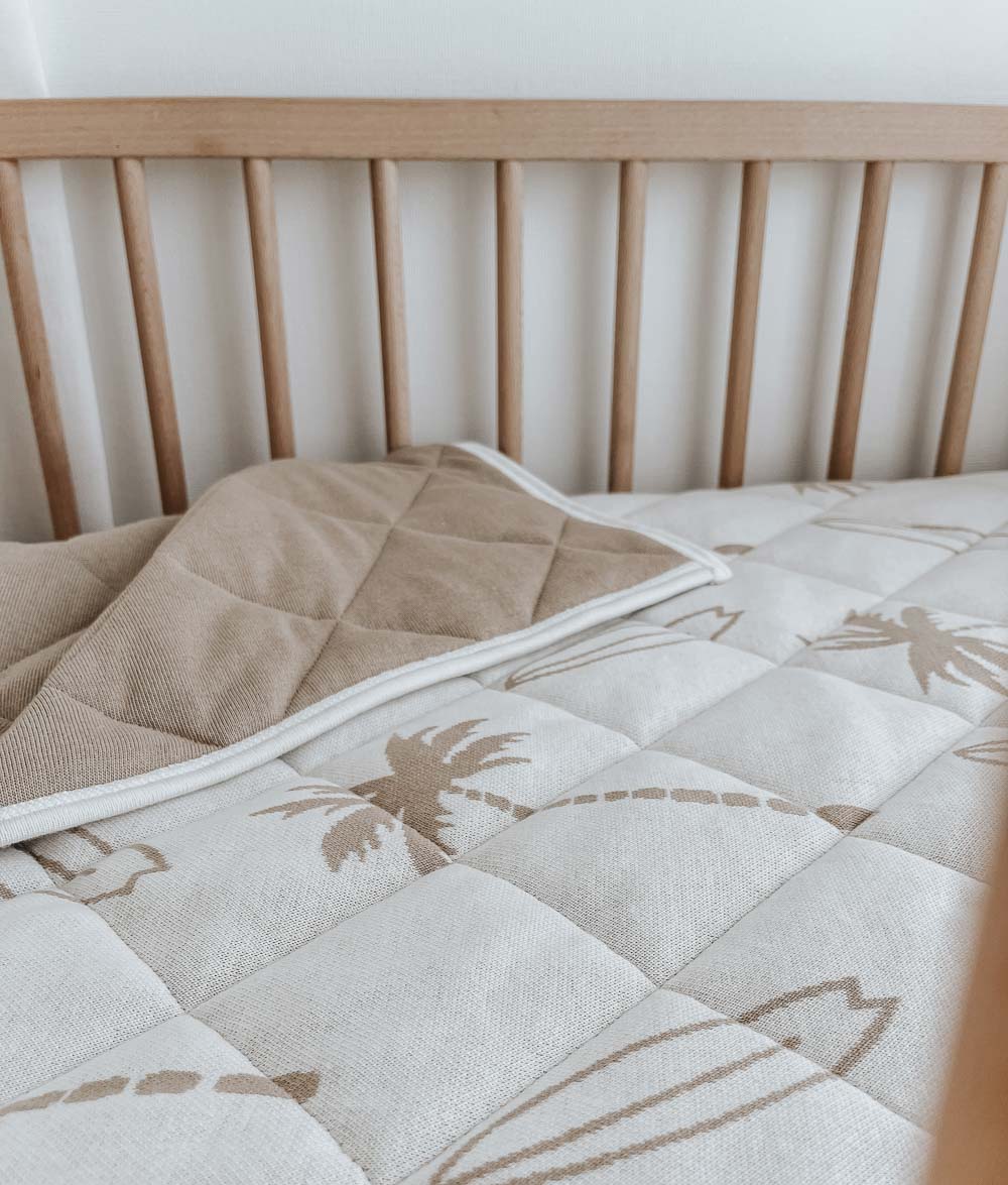 Surfing Palm reversible quilt in a timber cot, one corner folded to show the plain sand quilted side