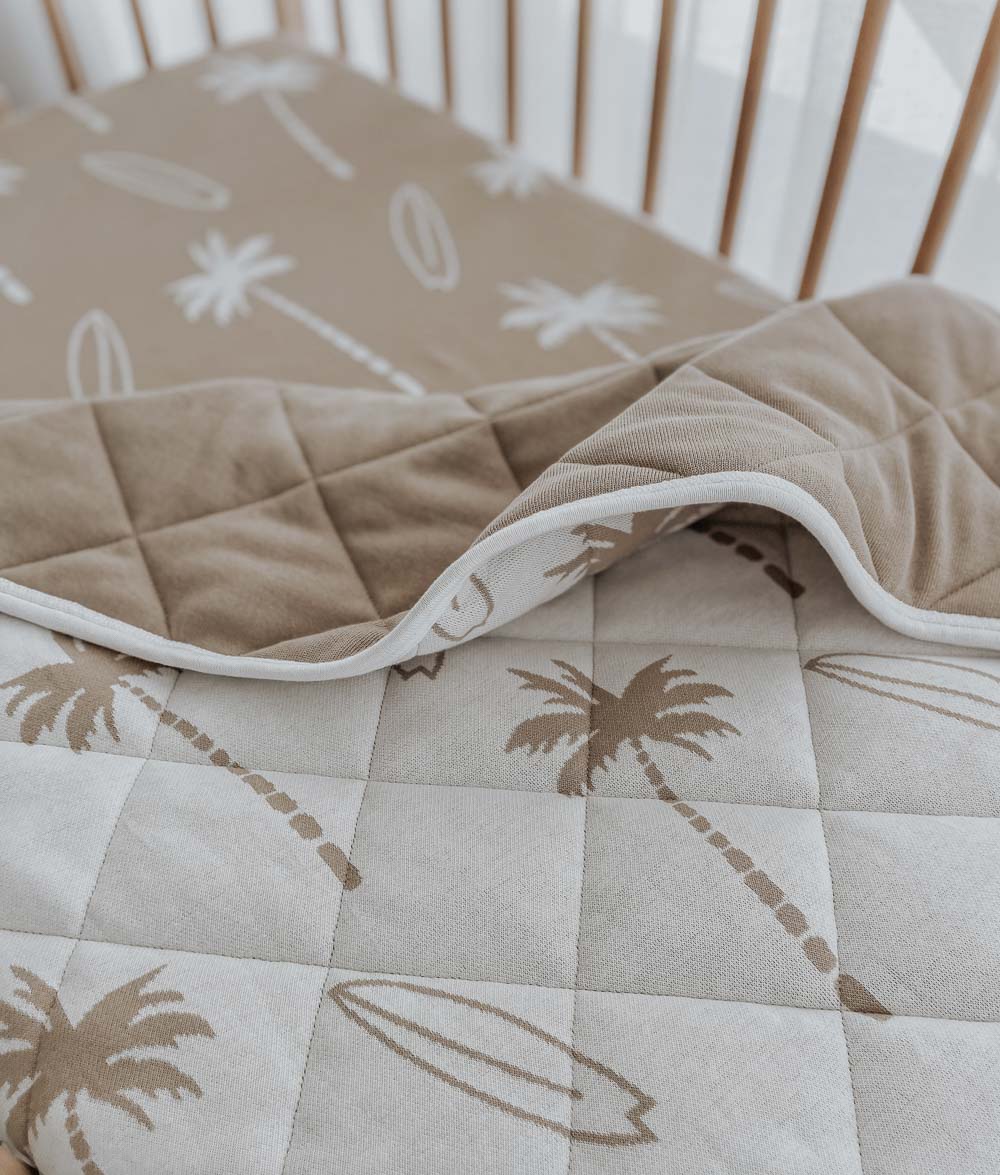 Sand Surfing Palm jersey cot sheet in a timber cot under a folded Surfing Palm quilt