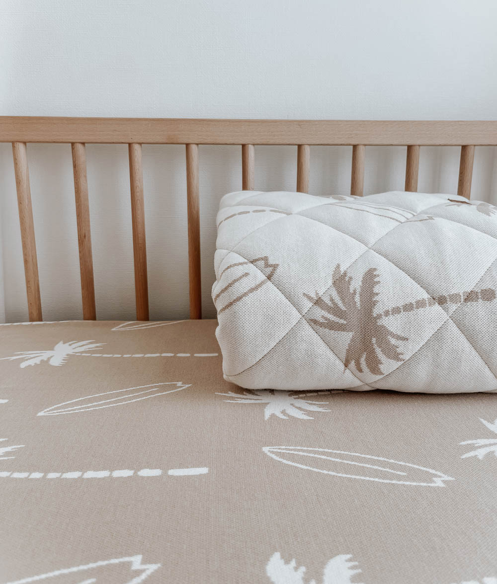 Sand Surfing Palm jersey cot sheet in a timber cot with a rolled Surfing Palm quilt