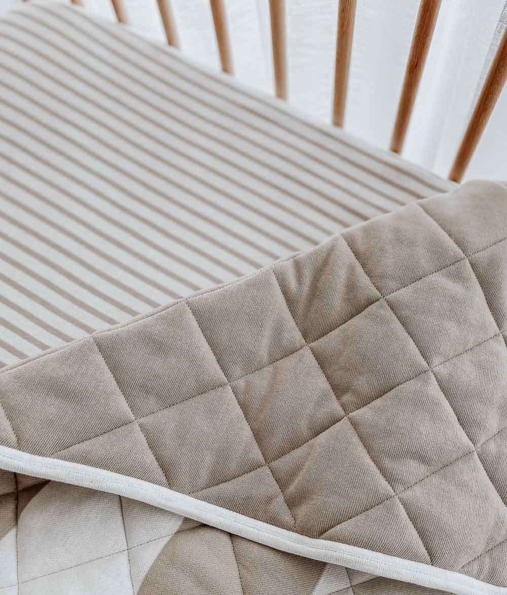 Greige stripe quilt folded back to its plain side on a greige pinstripe jersey cot sheet