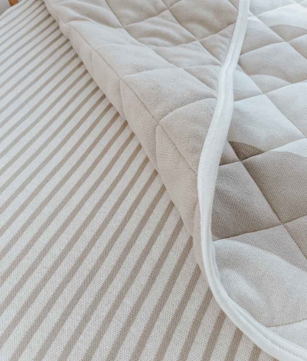 Close-up of the greige pinstripe jersey fitted sheet beneath the quilted edge of a greige quilt
