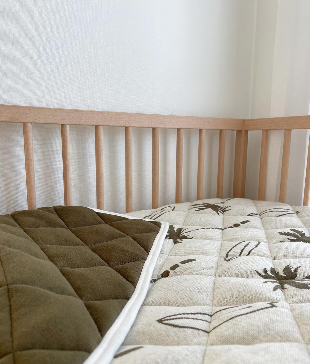 Olive Surfing Palm reversible quilt in a timber cot, turned back to show the plain olive side