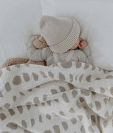 A baby sleeping in a MOON PHASE BLANKET from Bengali Collections with a teddy bear.