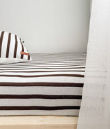 Striped bedding on a timber bed frame beside a sheer ivory curtain
