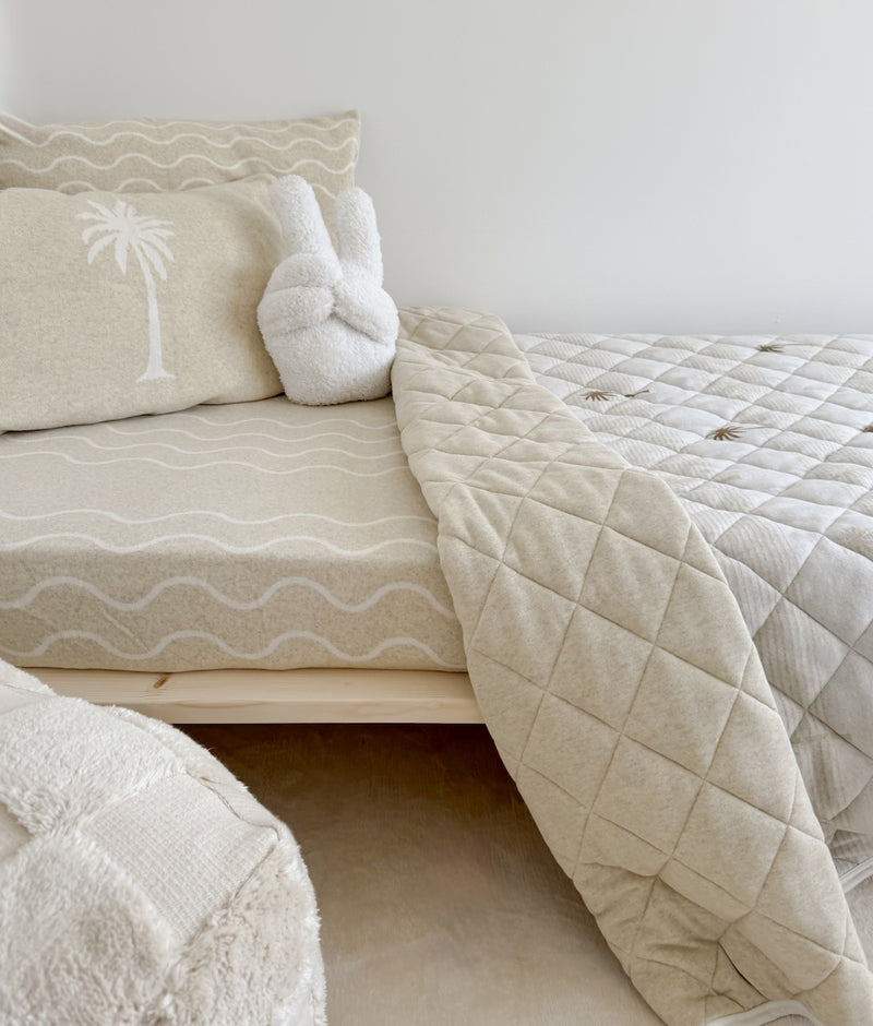 Kids bed with the Peace Sherpa cushion propped against a palm tree pillowcase beside a quilted throw
