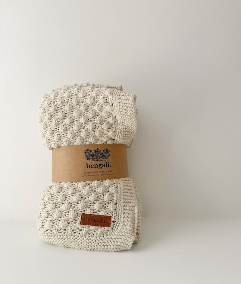 Folded Bone Popcorn knit throw showing its bobble texture and ribbed border, wrapped in a kraft Bengali band