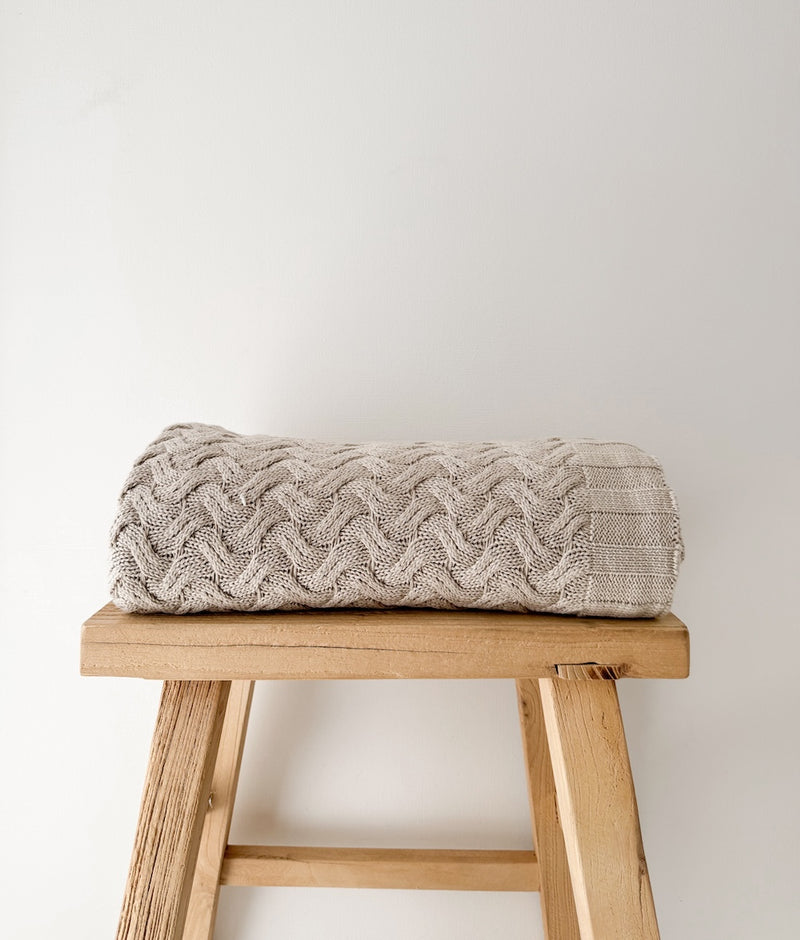 Folded Greige Wave knit cotton throw on a rustic timber stool