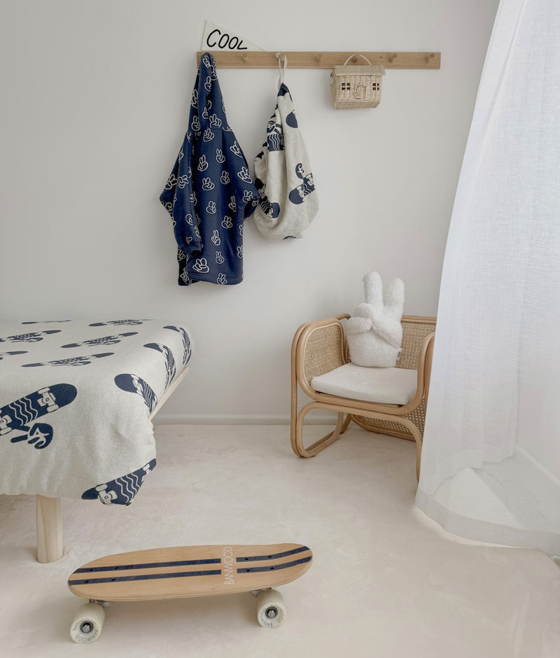 Kids room with the Peace Sherpa cushion on a small rattan chair, a skateboard and robes on wall hooks