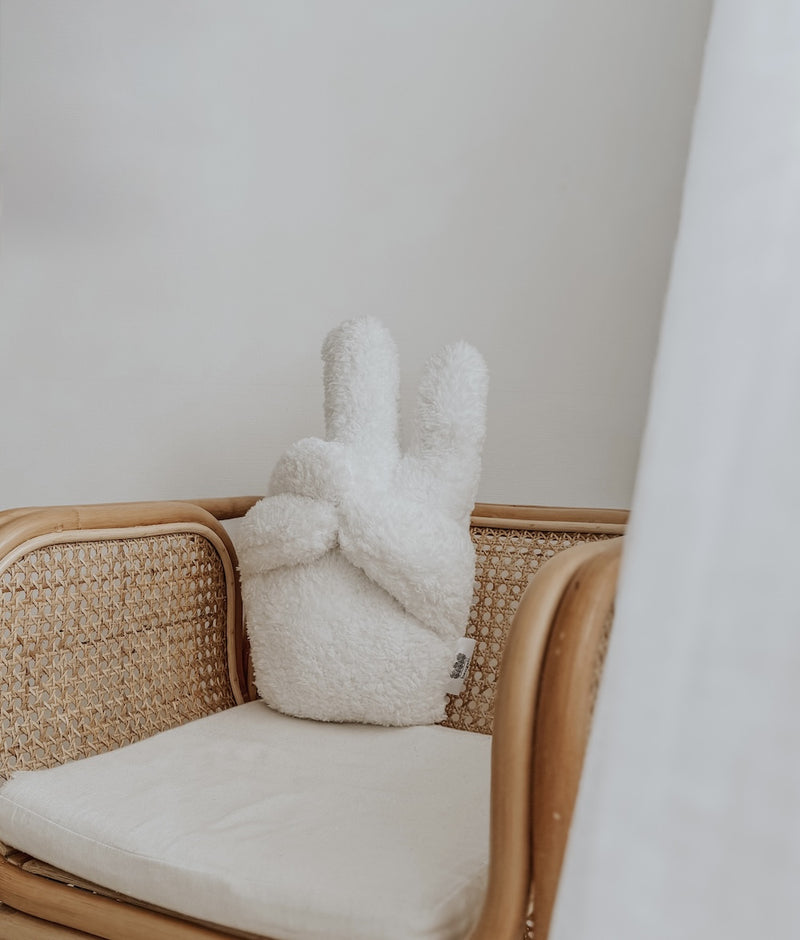 Ivory Peace Sherpa kids cushion sitting on a rattan armchair beside a sheer curtain