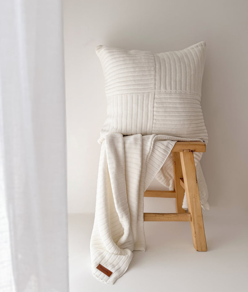 Ivory Corduroy knit cotton throw draped over a timber stool beneath a textured ivory cushion
