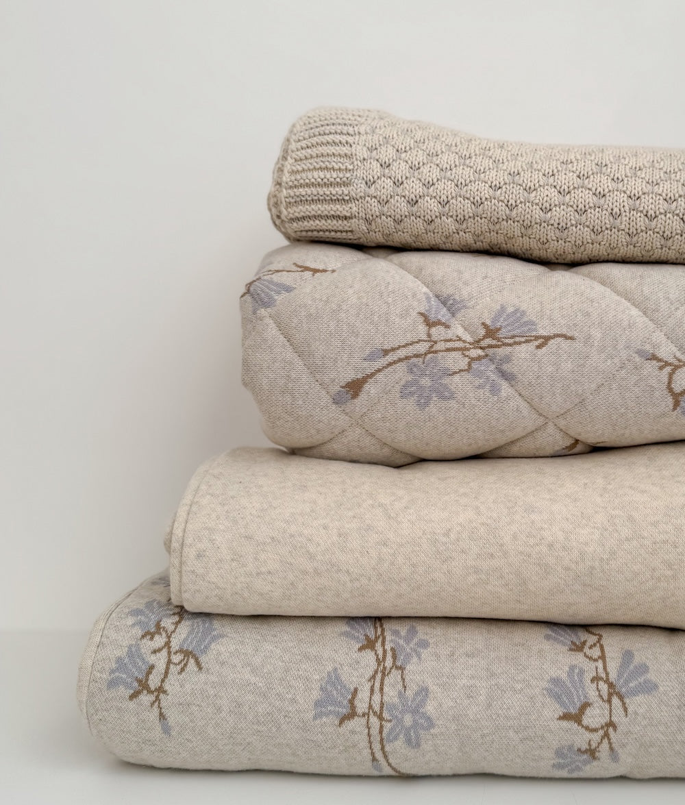Folded vanilla marle pebble blanket on top of a stack of quilted floral bedding