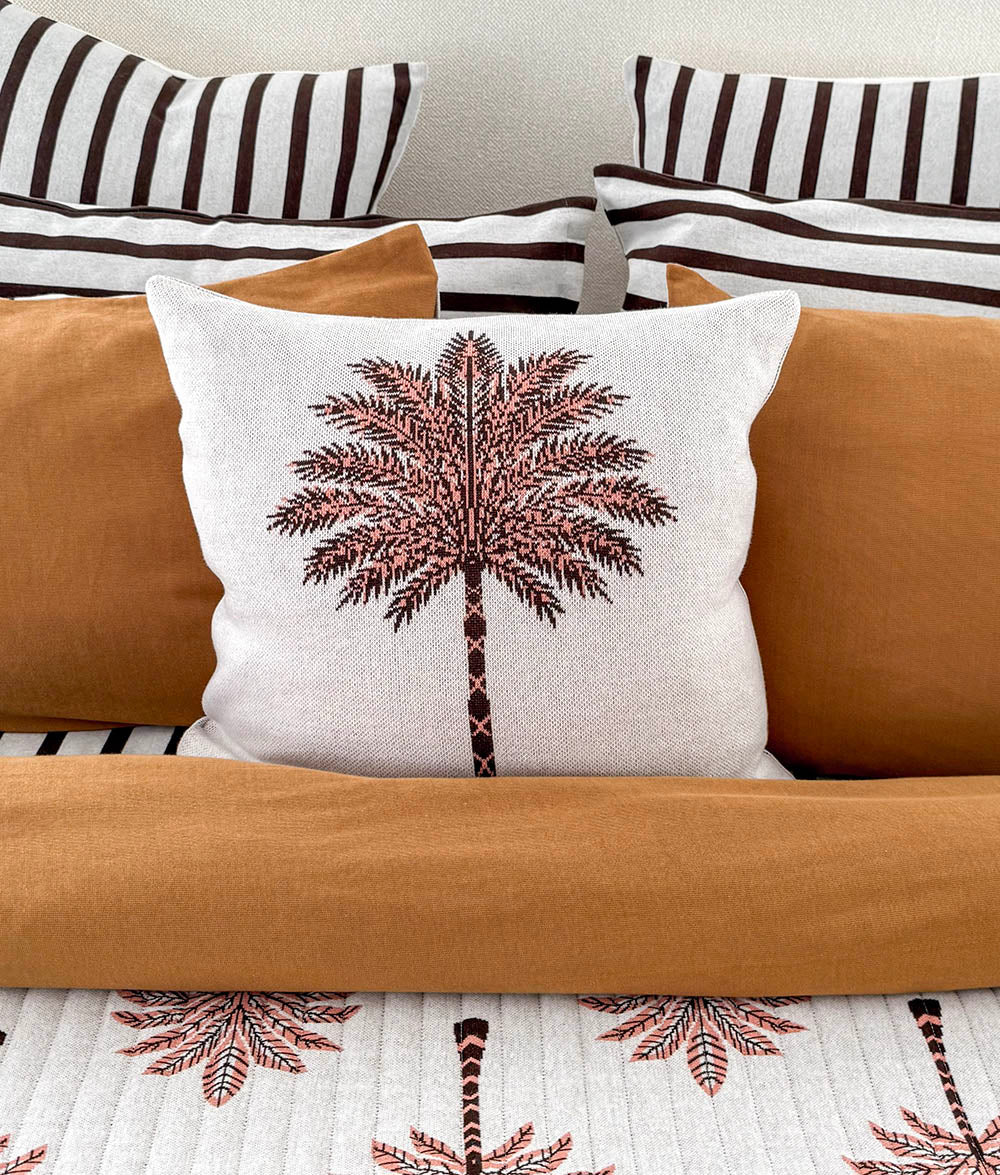 Palm print cushion on a tobacco quilt with striped euro pillowcases layered behind