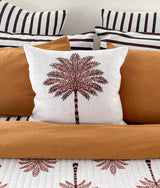 Palm print cushion on a tobacco quilt with striped euro pillowcases layered behind
