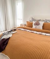 Bedroom with a tobacco quilted bed and chocolate and ivory striped pillows at the head