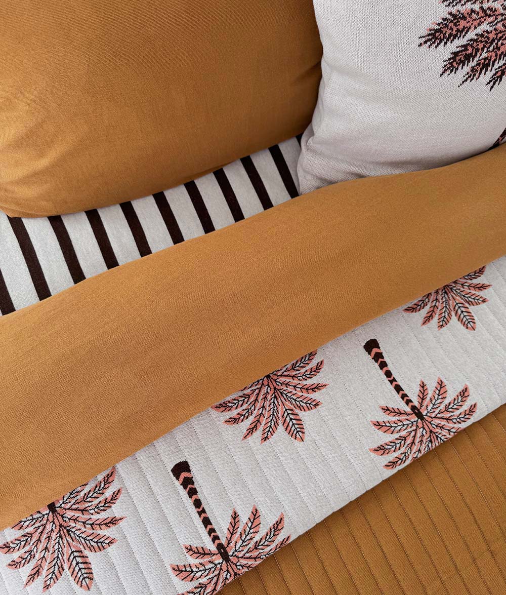 Tobacco quilt folded over palm print bedding with striped Sundown pillows behind