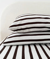 Striped jersey pillowcase stacked on a striped bed against an ivory curved headboard
