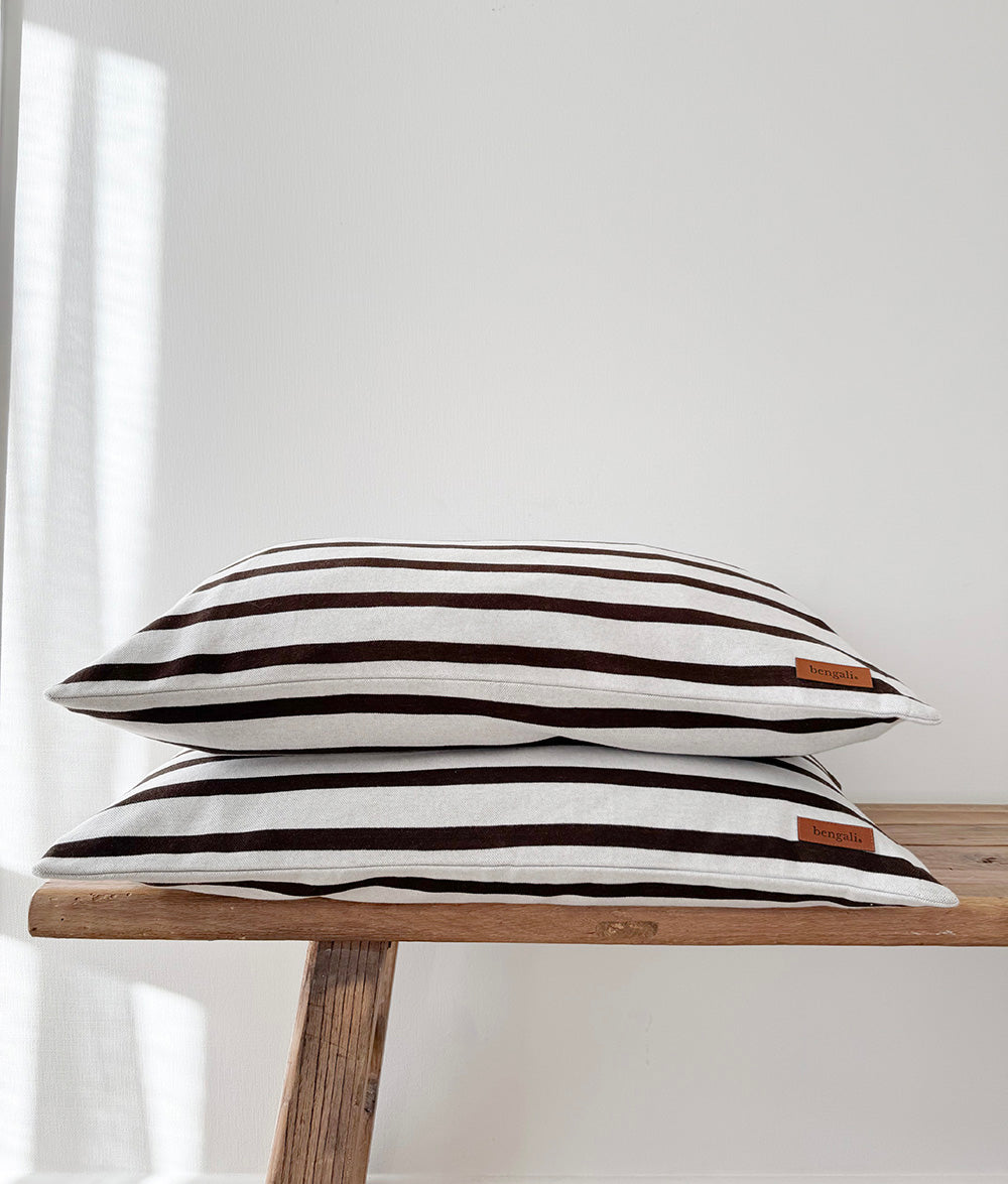 Two chocolate and ivory striped jersey pillowcases stacked on a timber bench