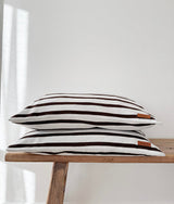Two chocolate and ivory striped jersey pillowcases stacked on a timber bench