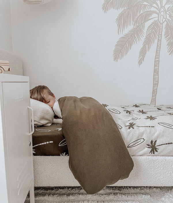 A child sleeping in a bed with a Surfing Palm duvet cover by Bengali Collections on the wall.