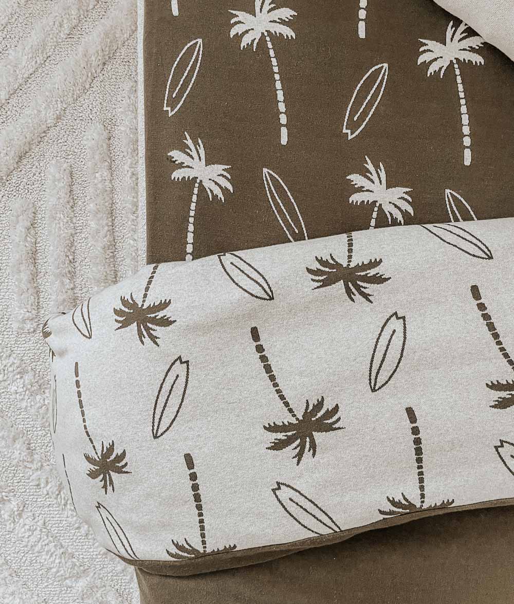 Folded Surfing Palm duvet cover in natural resting on an olive Surfing Palm jersey fitted sheet