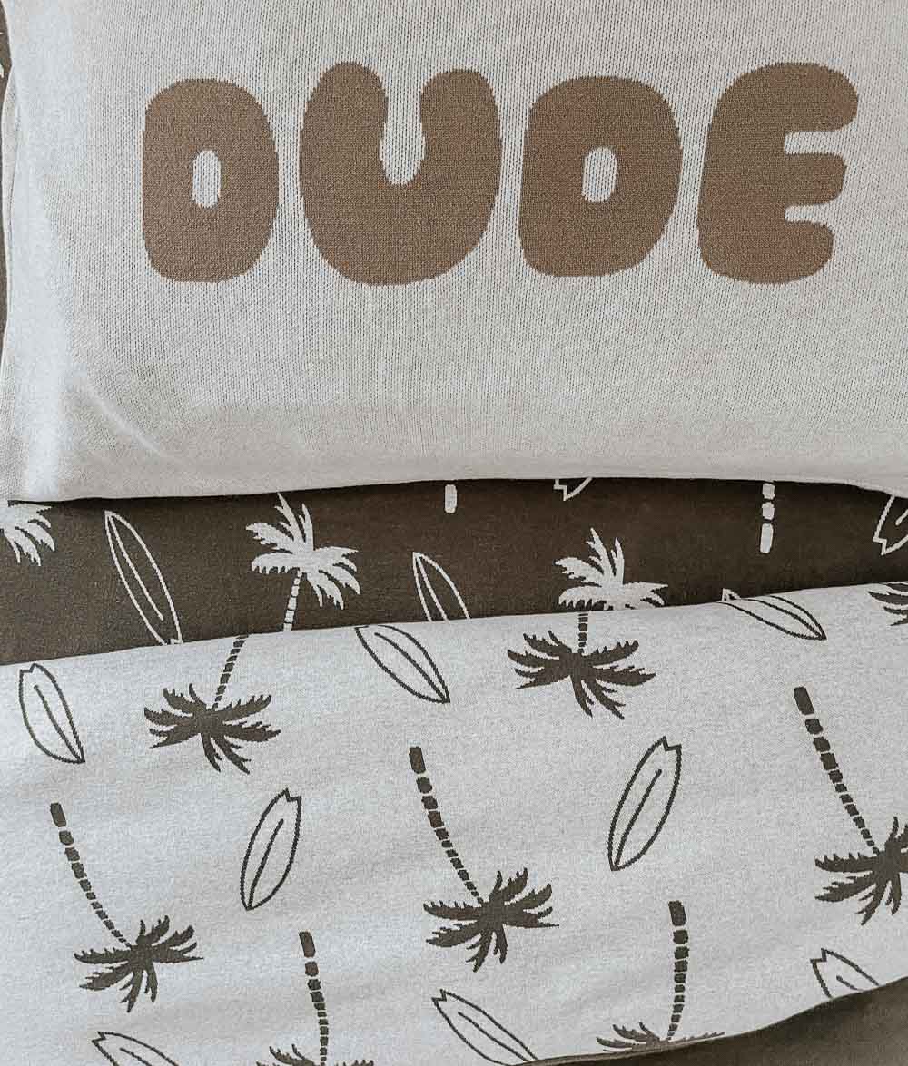 DUDE jersey pillowcase with sand lettering on top of folded Surfing Palm duvet covers in olive and natural