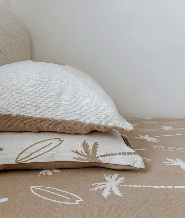 Natural Surfing Palm kids pillowcase under a plain pillow on a sand Surfing Palm jersey fitted sheet