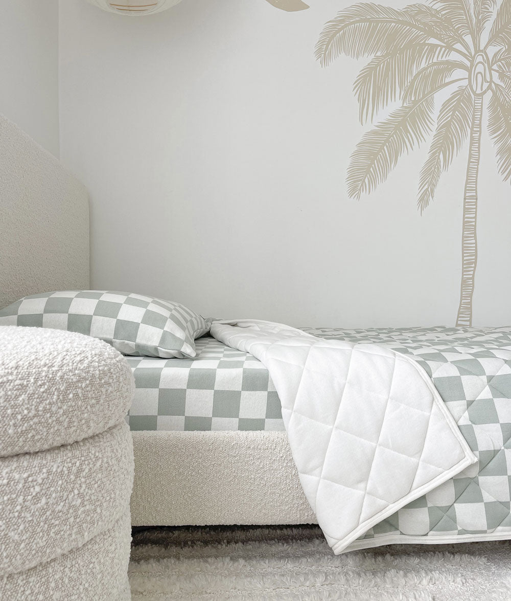 Sage Gingham reversible quilt folded back to its plain ivory side on a boucle bed beneath a palm mural