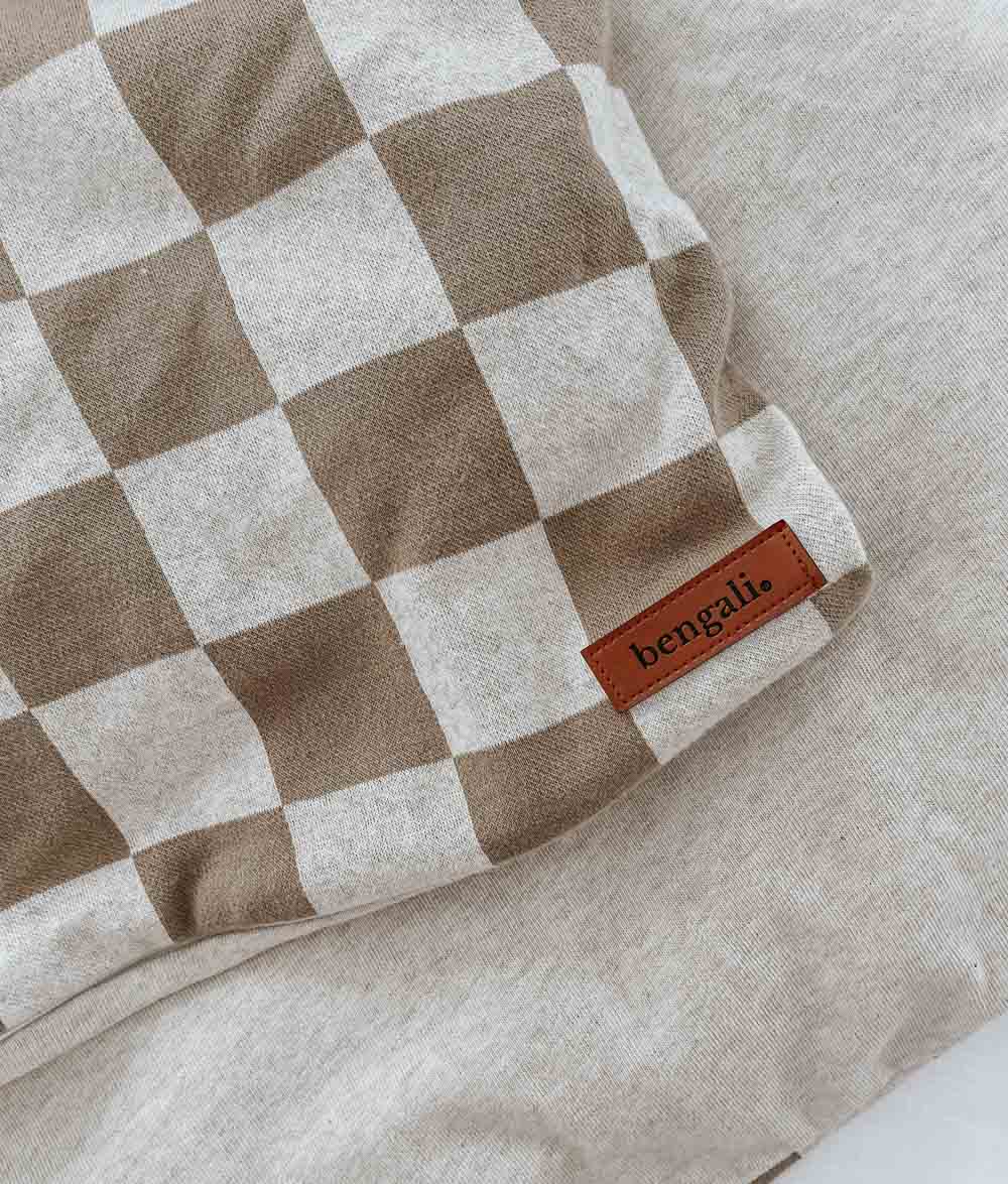 Corner of a khaki gingham jersey duvet cover with a leather Bengali label, on natural marle bedding