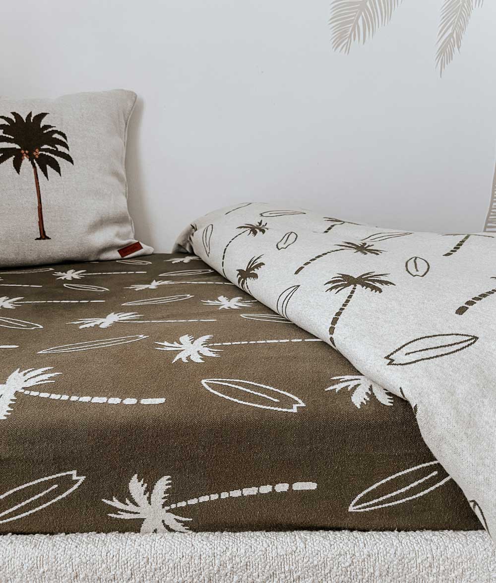 Olive Surfing Palm jersey fitted sheet on a kids bed with a natural duvet cover folded back and a palm tree cushion