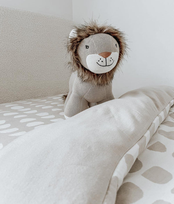 A Bengali Collections stuffed lion toy sits on top of a bed.