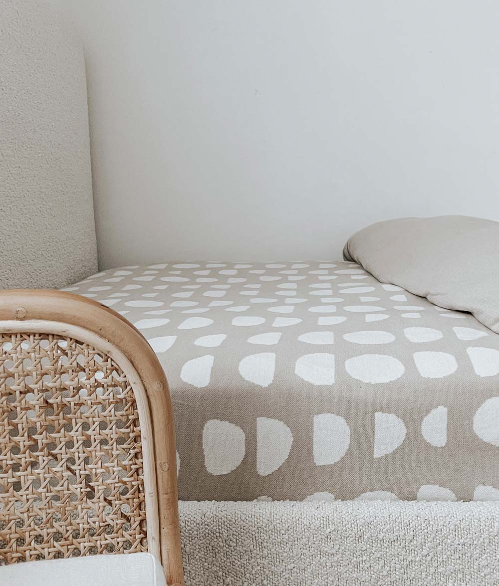 Moon Phase jersey fitted sheet in oatmeal with an ivory moon phase print on a boucle bed with a rattan end