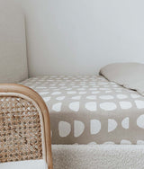A bed with a Jersey Cotton Sheet - Moon Phase from Bengali Collections and a wicker chair.