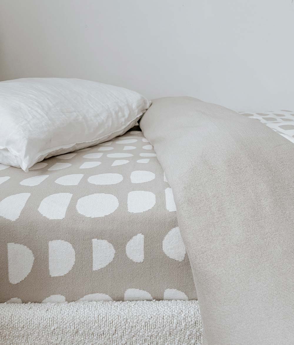 Moon Phase jersey cotton fitted sheet with a white pillow and folded oatmeal throw on a boucle bed