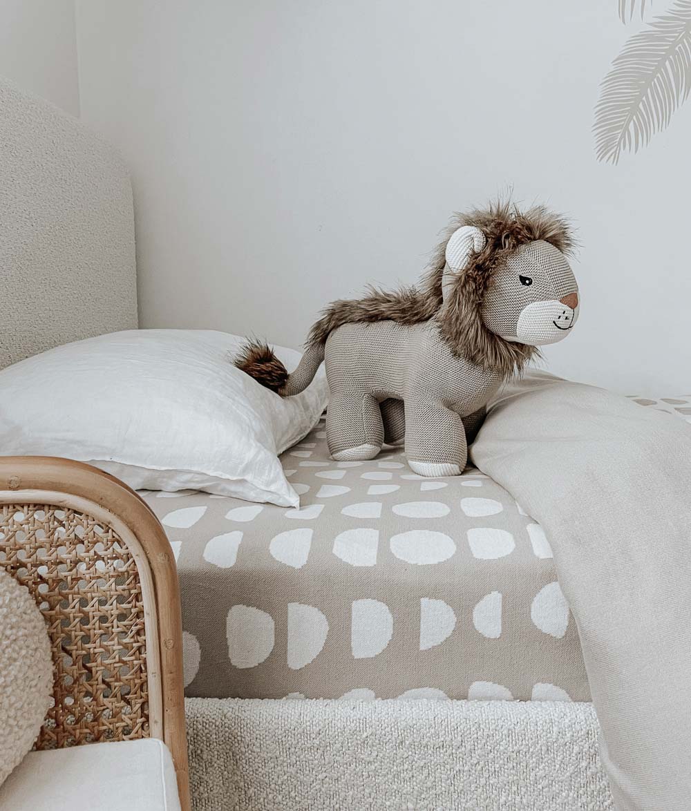 Knitted lion toy on a bed made up with a Moon Phase jersey fitted sheet and a white pillow