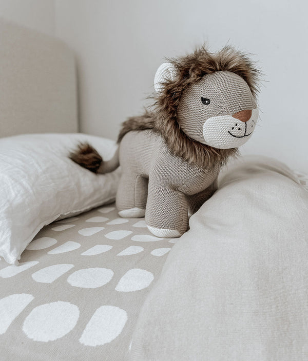A Bengali Collections lion toy sits on a bed in a bedroom.