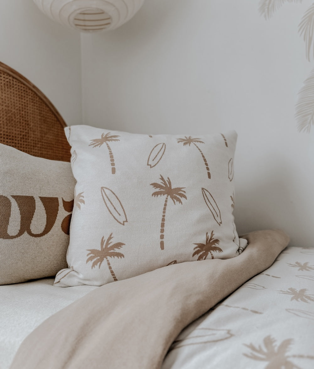 Ivory palm and surfboard print euro pillowcase on a bed beside a rattan headboard