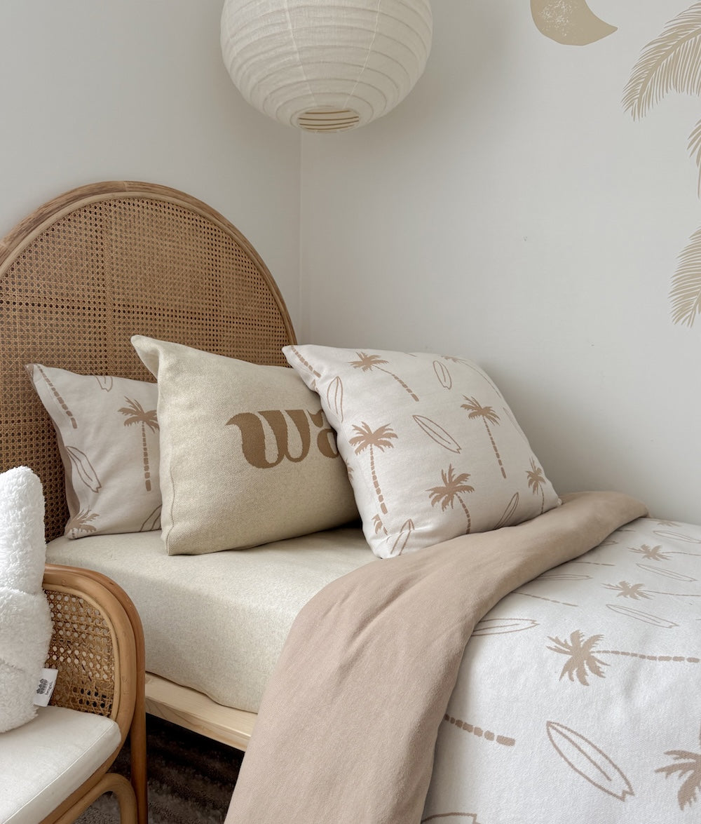 Kids bed with a rattan headboard, palm print euro pillowcase and a wave lettering cushion