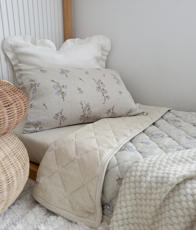 Ivory Frill euro pillowcase behind a bluebell print pillowcase on a quilted bed with a knit throw