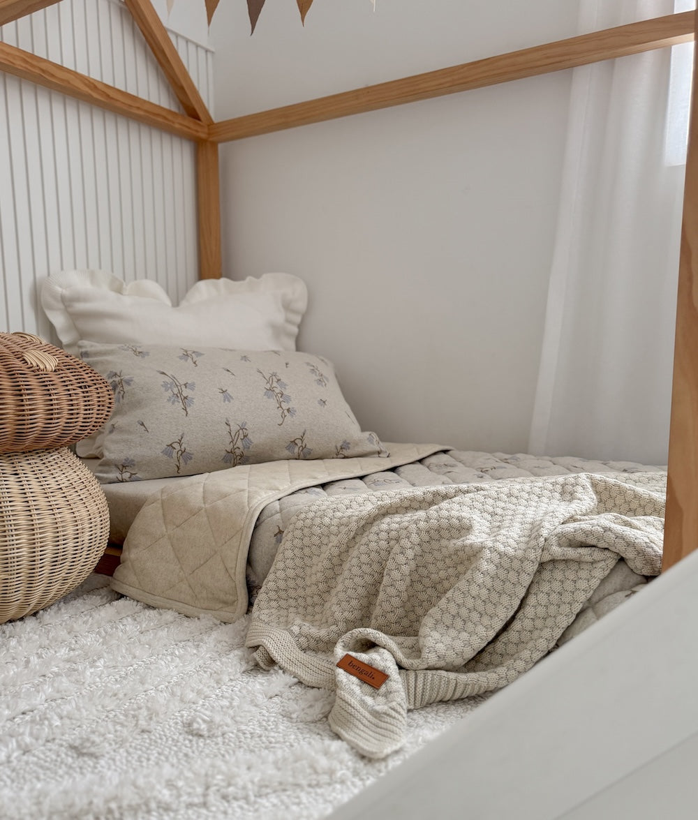 Pebble knit blanket on a house frame toddler bed beside a rattan mushroom stool