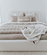 Bed with a high tide lumbar cushion, dune palm pillows and a quilted throw